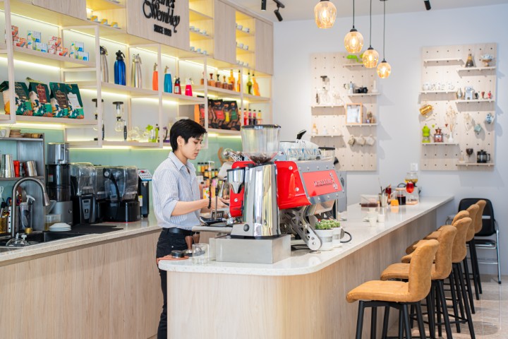 Charles Wembley barista team demonstrating coffee preparation techniques at a training counter, group smiling and attentive, modern café environment, energetic and welcoming mood